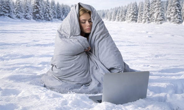 Person wrapped in a blanket in the snow with a laptop.
