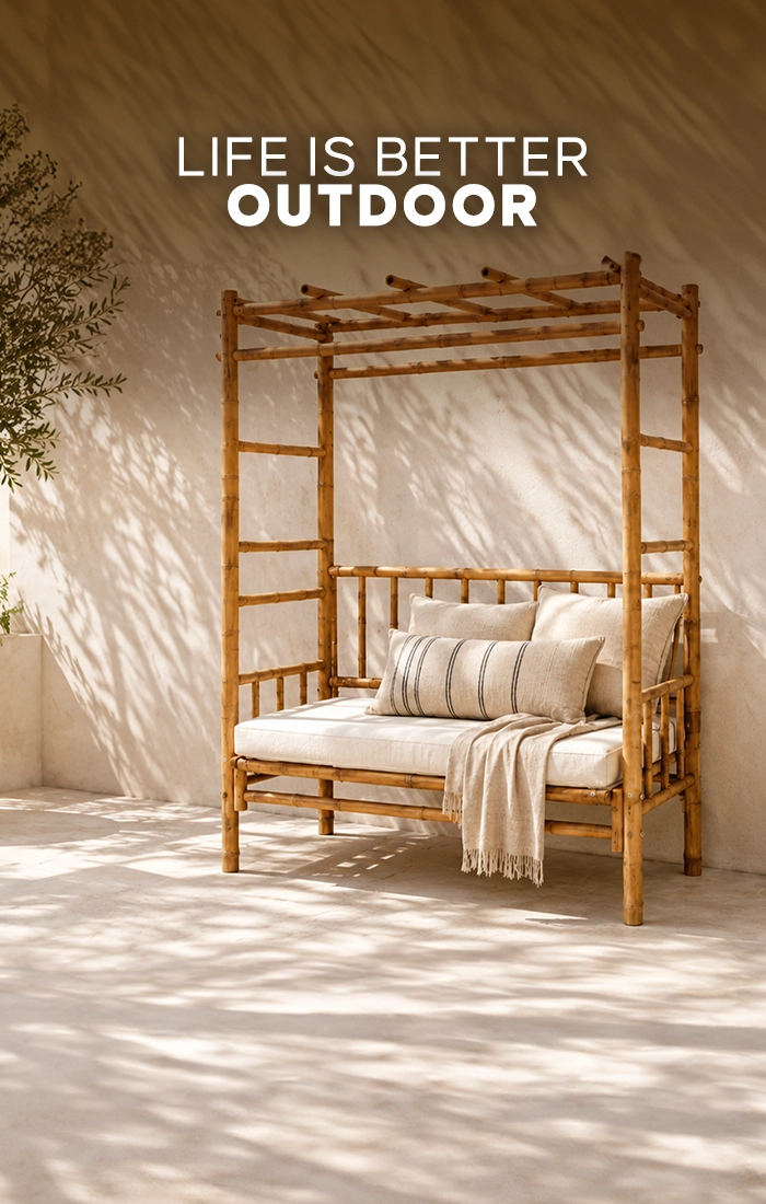 Natural bamboo outdoor daybed with cream cushions and a beige throw on a sunlit Mediterranean terrace.