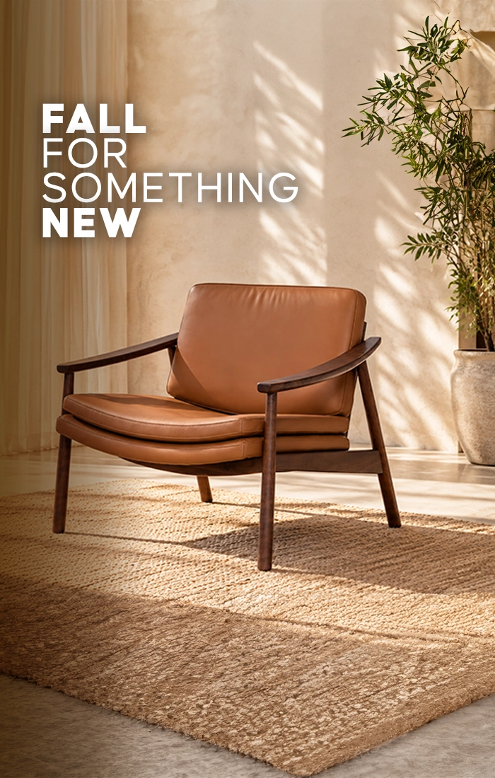 Modern brown leather armchair with wooden frame on a textured beige rug in a sunlit living room, featuring a potted olive tree and large windows.