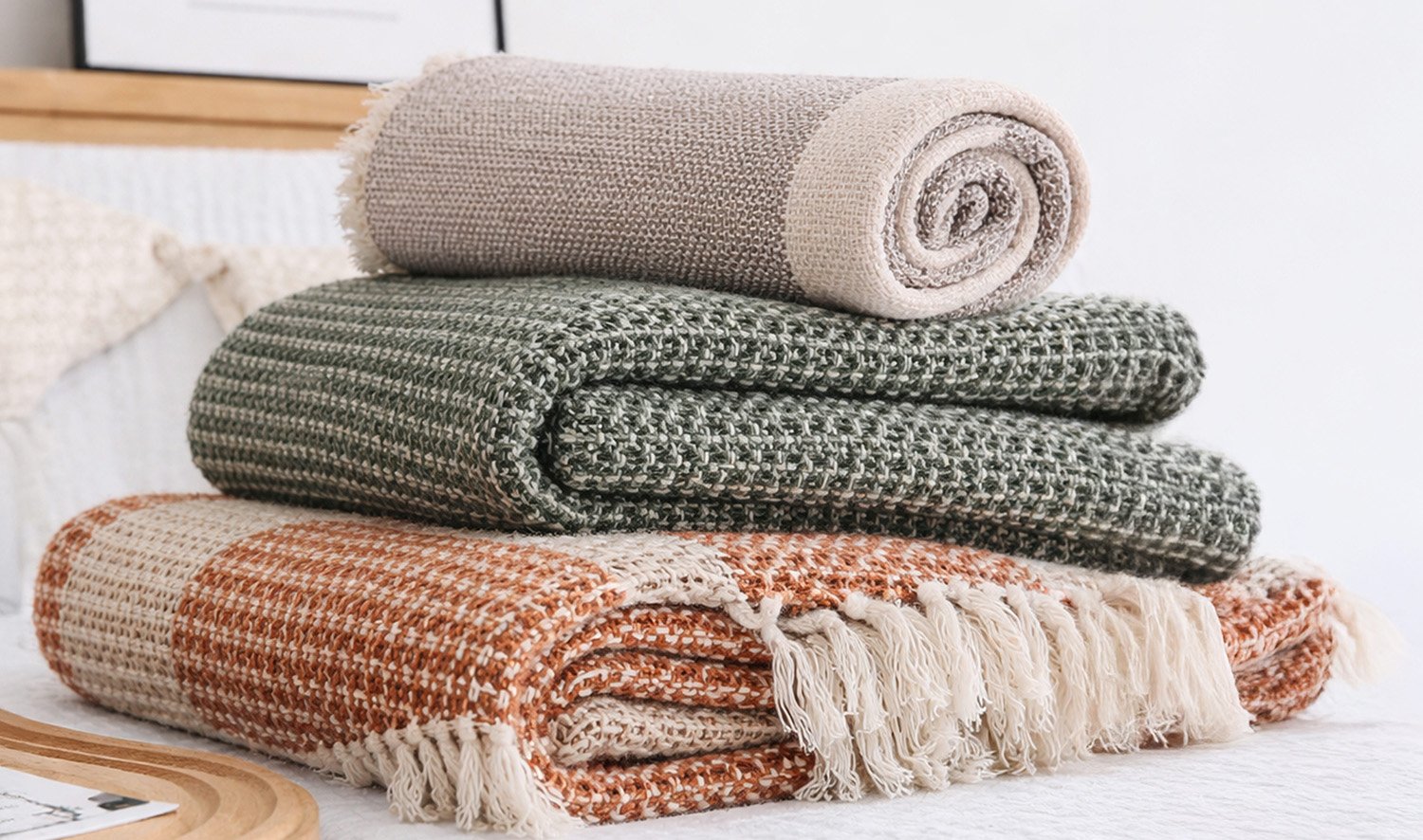 Stack of chunky woven throws in green and rust with a soft neutral top.